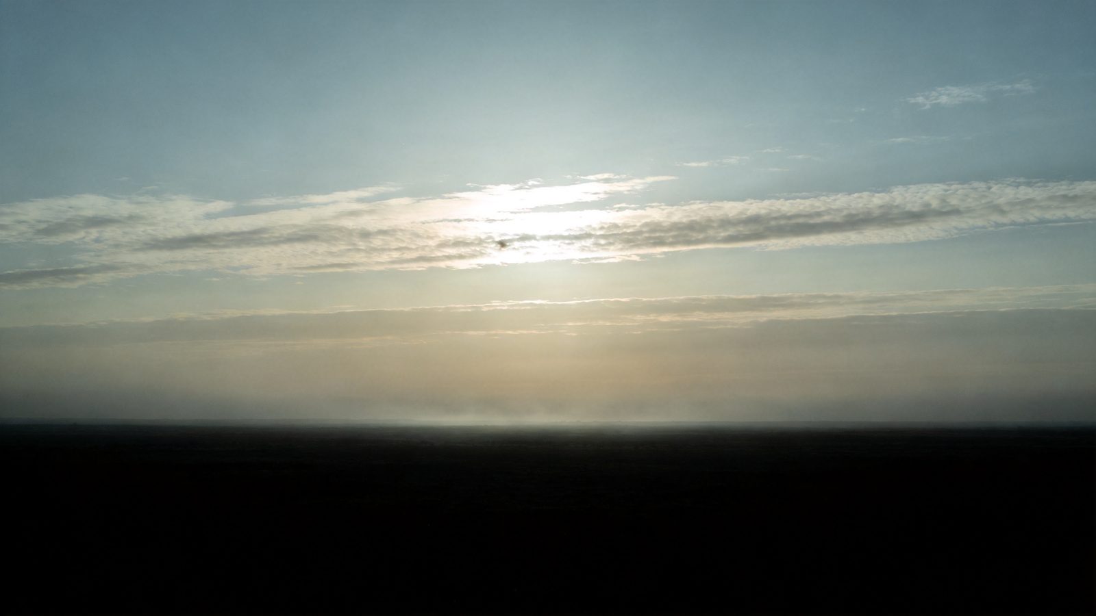 Atmospheric image: a clearing dawn sky, soft light breaking through thin high clouds over a wide dark horizon — symbolic of the clarity gained.